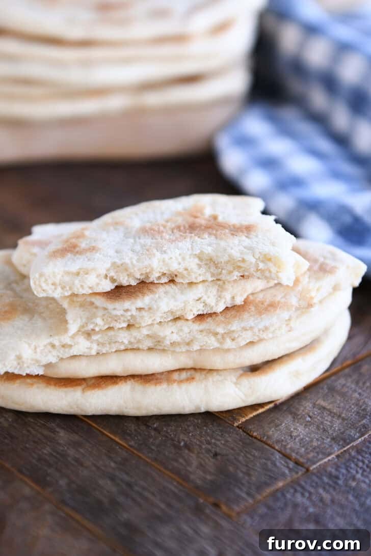 A stack of golden brown flatbreads on a wooden counter, with the top flatbread torn into pieces, revealing its soft interior.
