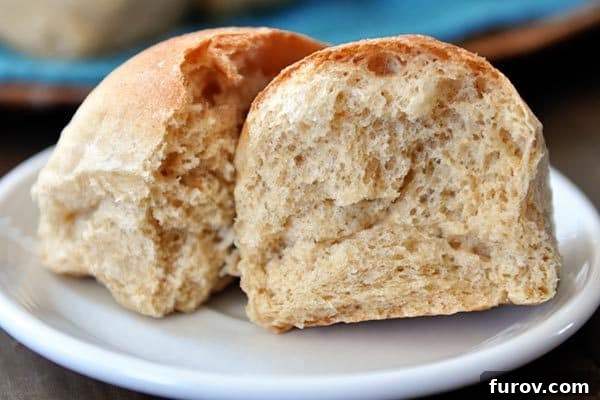 A perfectly baked whole wheat roll split in half on a white plate, revealing its soft, airy interior.