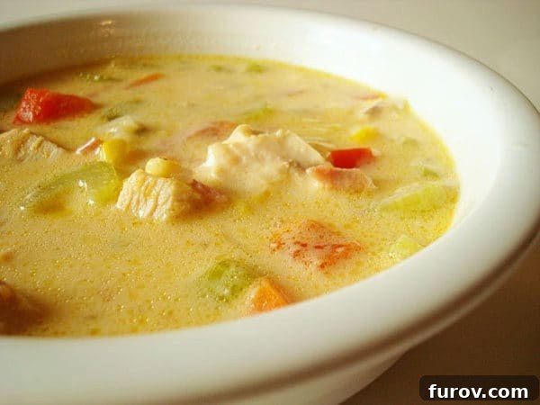 Chicken chowder with corn and chopped peppers in a white bowl.