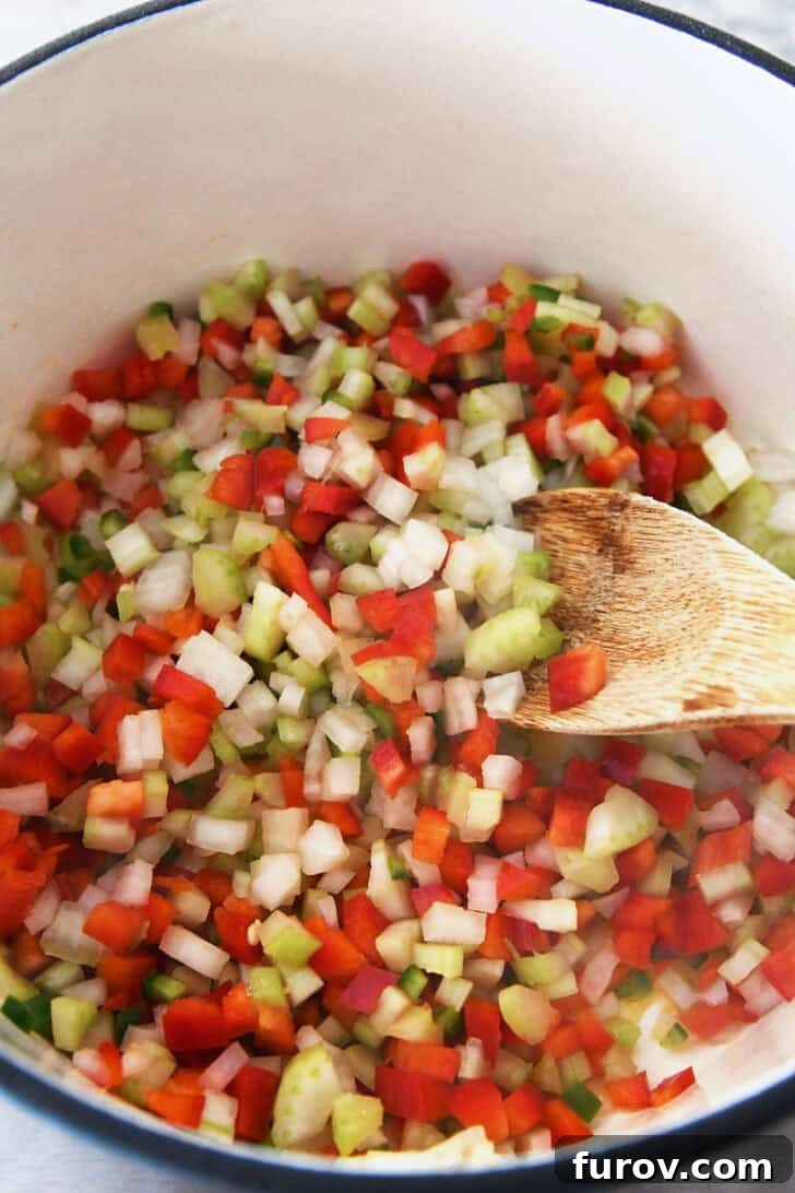Top down view of a pot with small diced vegetables and a wooden spoon.