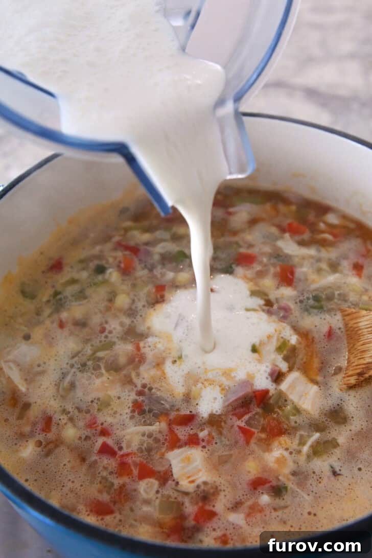 A milk mixture being poured into a pot of broth, chicken, and vegetables.