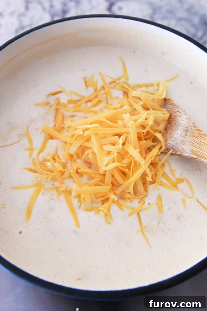 Top down view of a pot with a white creamy soup mixture and shredded cheddar cheese on top.