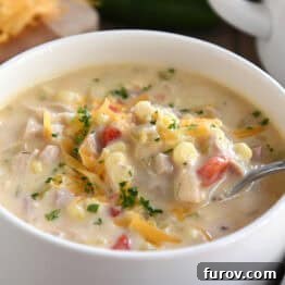 A white bowl with a spoon taking a bite of chicken corn chowder out of the bowl.