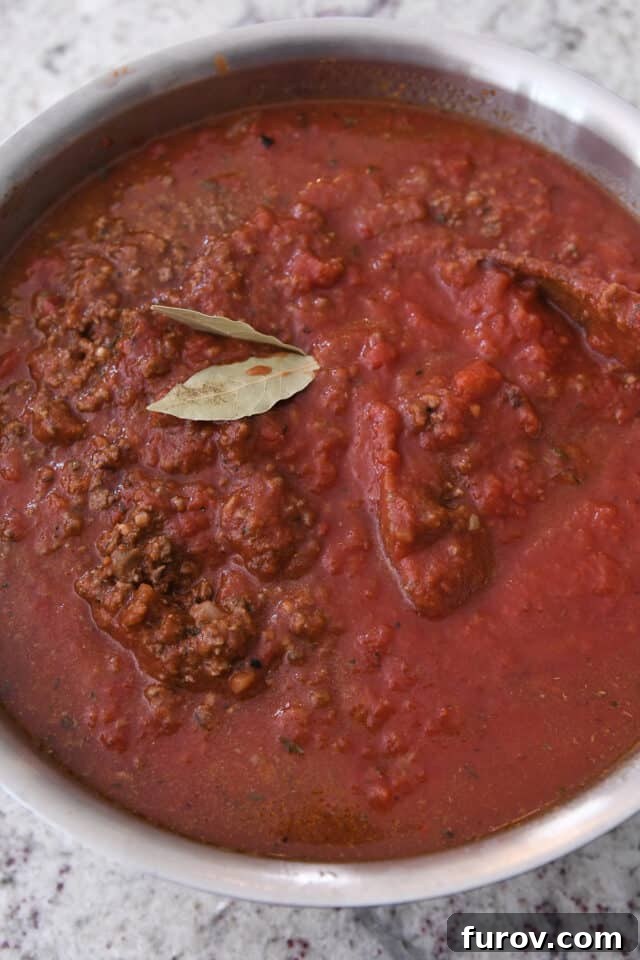 Pot with bubbling spaghetti sauce and two bay leaves visibly infusing flavor.