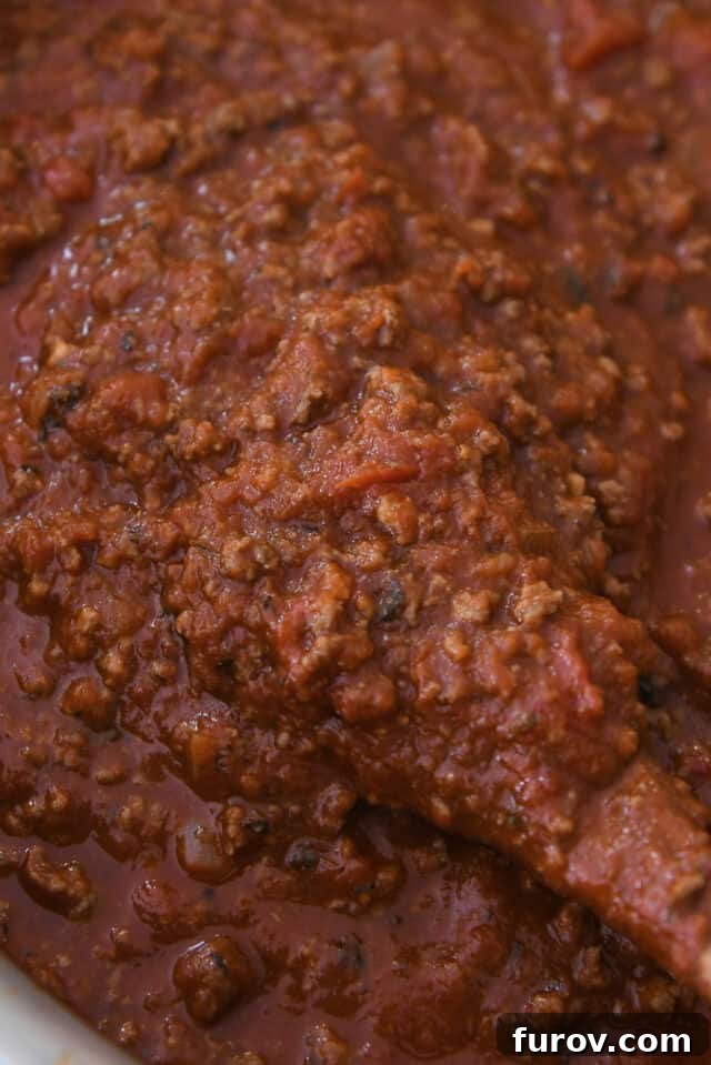 Wooden spoon stirring a pot of homemade spaghetti sauce, showing its rich texture.