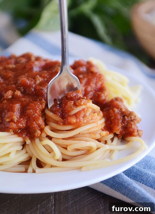 A fork twirling a bite of homemade spaghetti sauce and cooked spaghetti noodles, ready for a delicious taste.