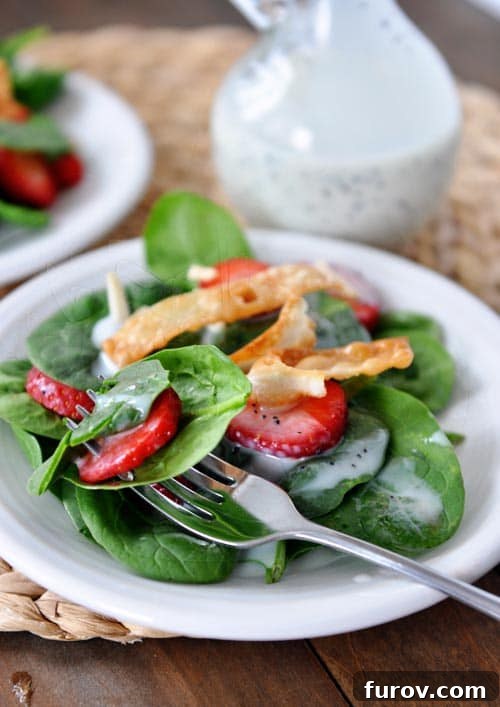 Juicy Strawberry Spinach Salad with Dreamy Poppy Seed Dressing 2 A beautifully presented white plate full of vibrant strawberry spinach salad, with a fork poised to take a bite. The creamy poppy seed dressing glistens.