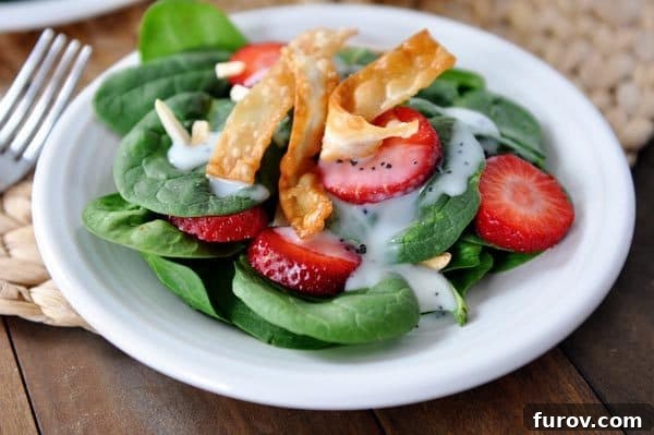 Juicy Strawberry Spinach Salad with Dreamy Poppy Seed Dressing 3 A close-up view of a fresh spinach strawberry salad, generously topped with homemade crispy wonton strips, served on a white plate.