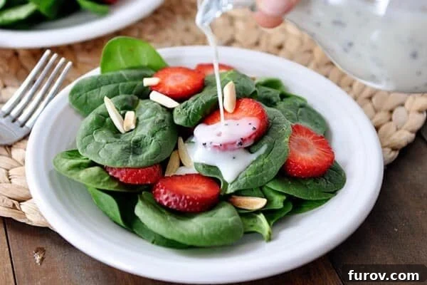 Juicy Strawberry Spinach Salad with Dreamy Poppy Seed Dressing 4 A hand gently pouring the luscious homemade creamy poppy seed dressing over a bowl of fresh spinach strawberry salad, ready to be enjoyed.