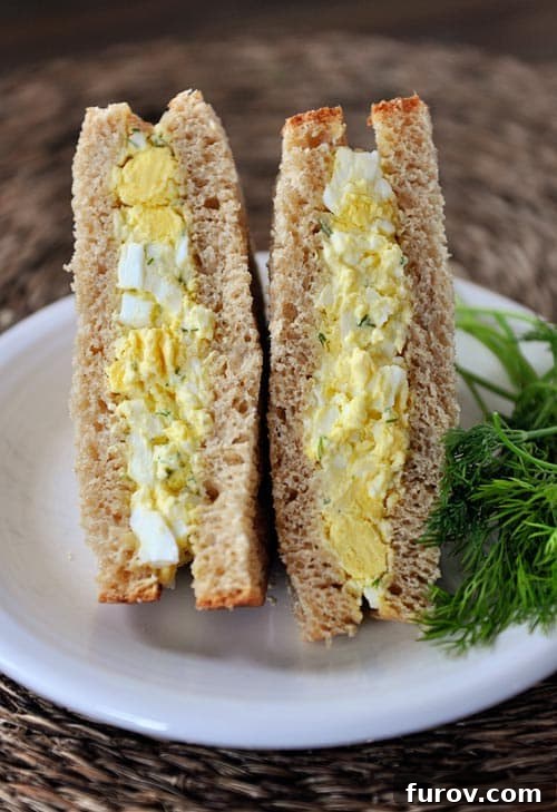An egg salad sandwich cut in half on a white plate, showcasing a creamy, delicious filling.