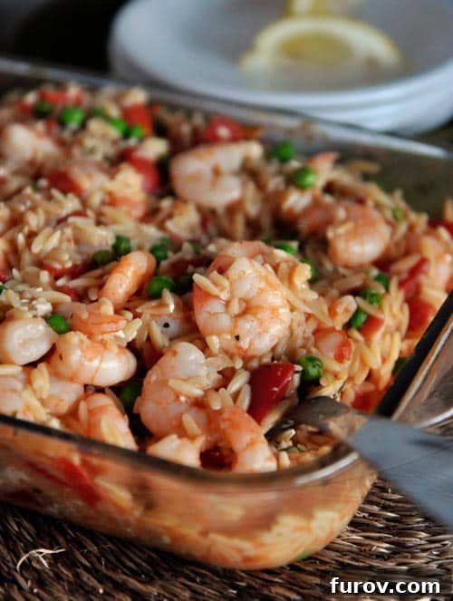 A vibrant glass baking dish brimming with baked shrimp, orzo pasta, green peas, and diced tomatoes, ready to be served.