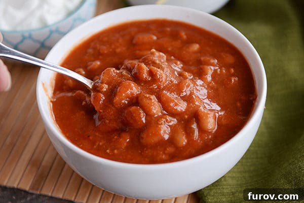 Mom's Hearty Chili: Perfect for Stovetop or Slow Cooker 3 A white bowl full of rich red chili with a spoon resting in it, ready for serving.