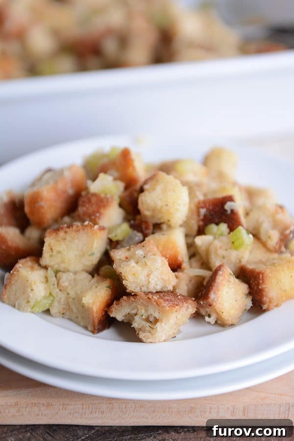 A close-up of a white plate holding a generous serving of Thanksgiving stuffing, showing its golden-brown crust.