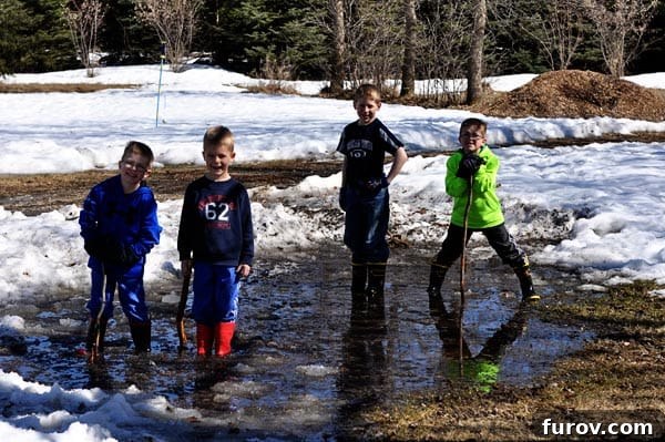 four young boys enthusiastically playing in icy, muddy water, embracing outdoor fun