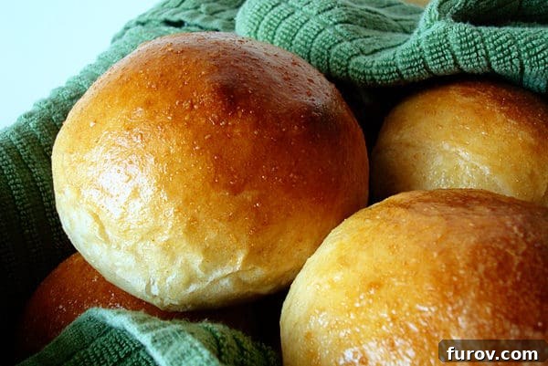 An overhead shot of several golden brown, perfectly baked dinner rolls arranged neatly on a green kitchen towel.