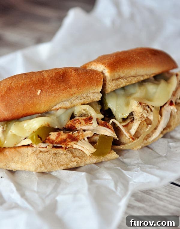 A perfectly assembled Slow Cooker Chicken Philly Sandwich, cut in half and resting on parchment paper, showcasing tender chicken, peppers, onions, and melted provolone cheese.