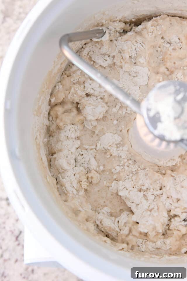 Fast and Flawless Pizza Dough 3 Warm water, all-purpose flour, and instant yeast being mixed in a stand mixer with a dough hook.