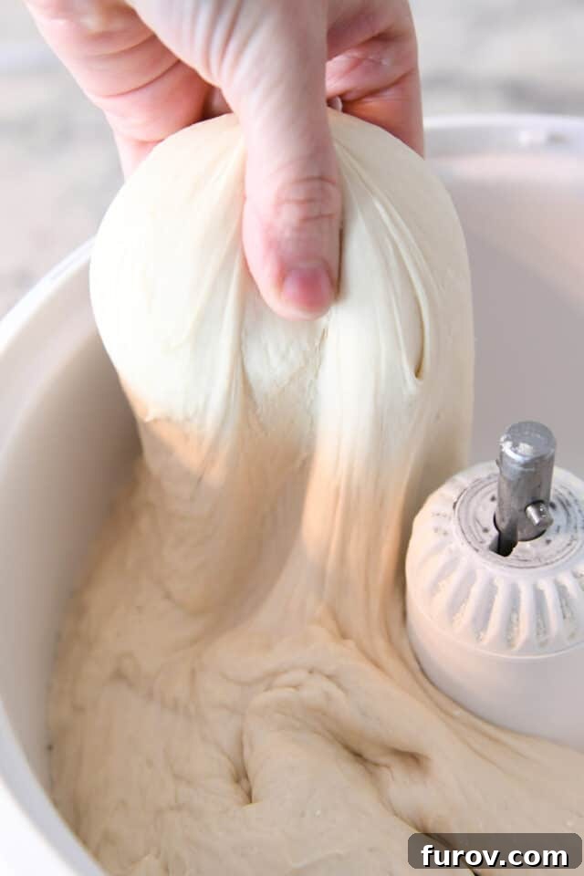 Fast and Flawless Pizza Dough 5 Soft, risen pizza dough being pulled from a stand mixer bowl, ready for shaping.