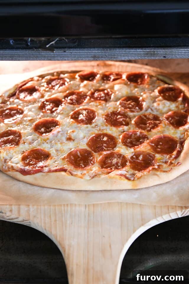 Fast and Flawless Pizza Dough 6 A freshly baked pepperoni pizza with a perfectly golden and bubbly crust being removed from the oven with a pizza peel.