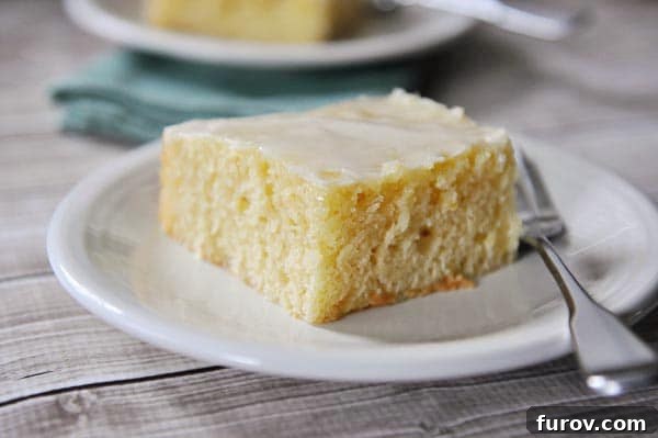 A square piece of glazed lemon sheet cake on a white plate, highlighting its tender texture.