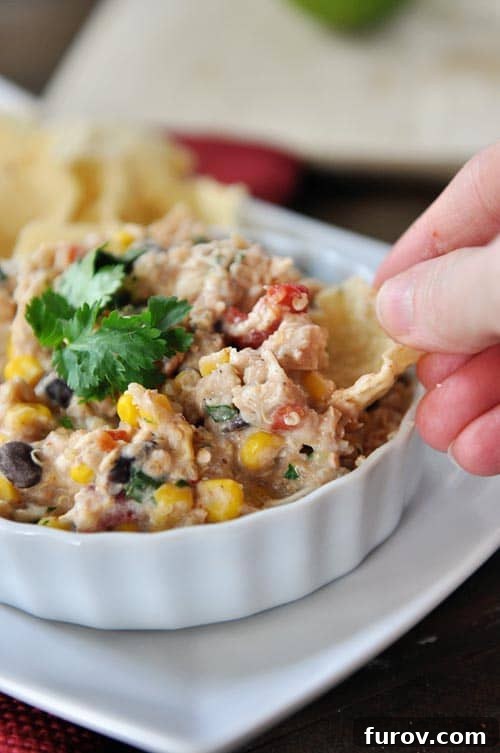 Cheesy Fiesta Quinoa Poppers 2 A tortilla chip being dipped into a white ramekin full of a creamy tex-mex quinoa mixture, showcasing its rich texture and appealing color.