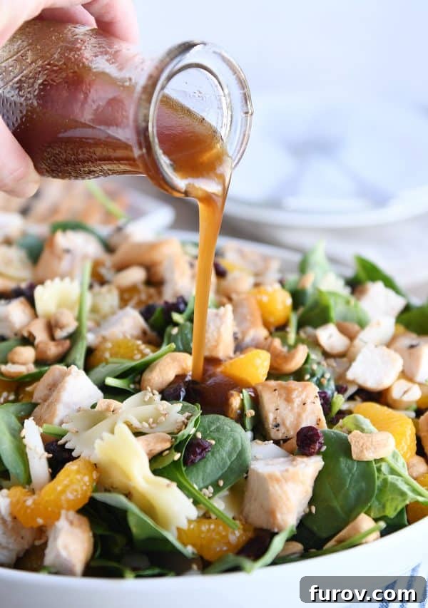 Teriyaki dressing being poured over a vibrant bowl of Mandarin Spinach Bowtie Pasta Salad.