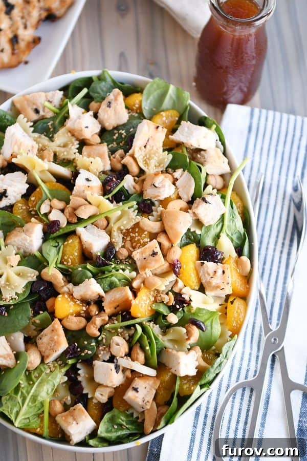 Top-down view of a large white bowl filled with Mandarin Spinach Bowtie Pasta Salad, glistening with teriyaki dressing.
