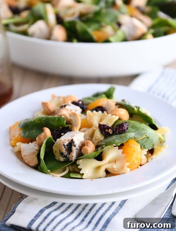 A generous serving of Mandarin Spinach Bowtie Pasta Salad on a white plate, ready to be enjoyed.