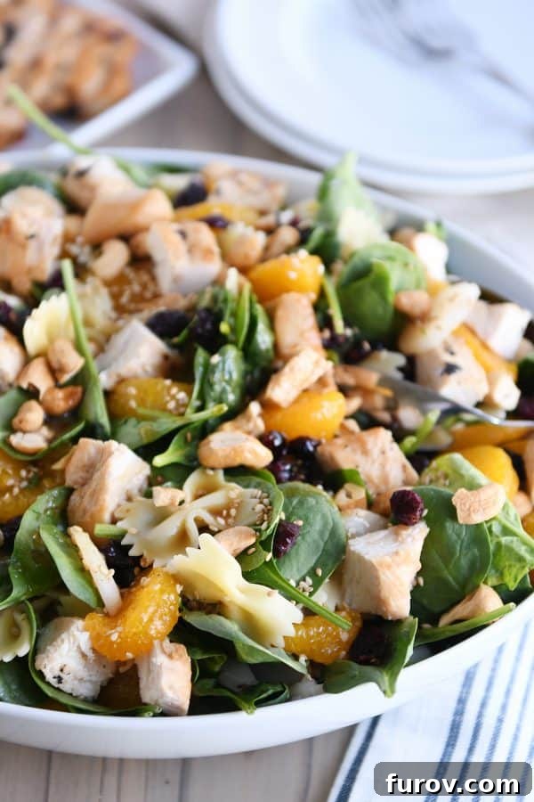 A full, large white bowl of Mandarin Spinach Bowtie Pasta Salad, showcasing its colorful ingredients.