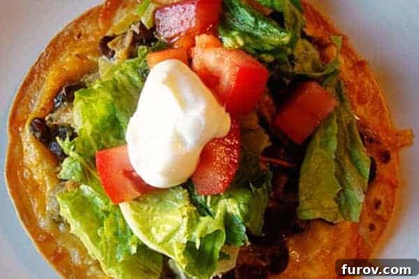 Top view of a tostada with all the toppings, including shredded chicken, black beans, lettuce, and sour cream.