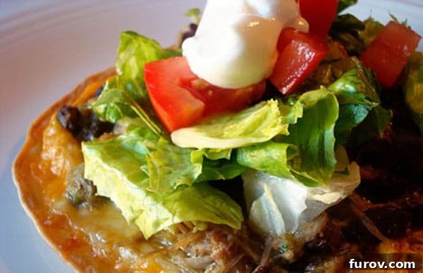 Close-up of a loaded tostada featuring fresh lettuce, juicy tomato, a dollop of sour cream, and creamy avocado slices.