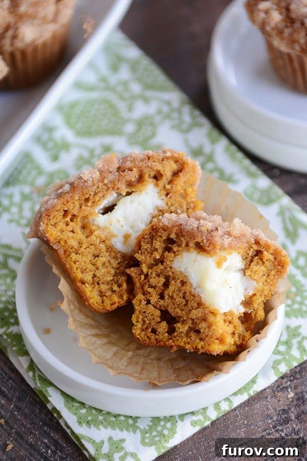 A cream cheese filled pumpkin muffin split in half on a white ramekin, showcasing the creamy center.