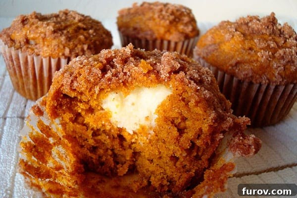 A partially eaten cream cheese filled pumpkin muffin in front of three other muffins.