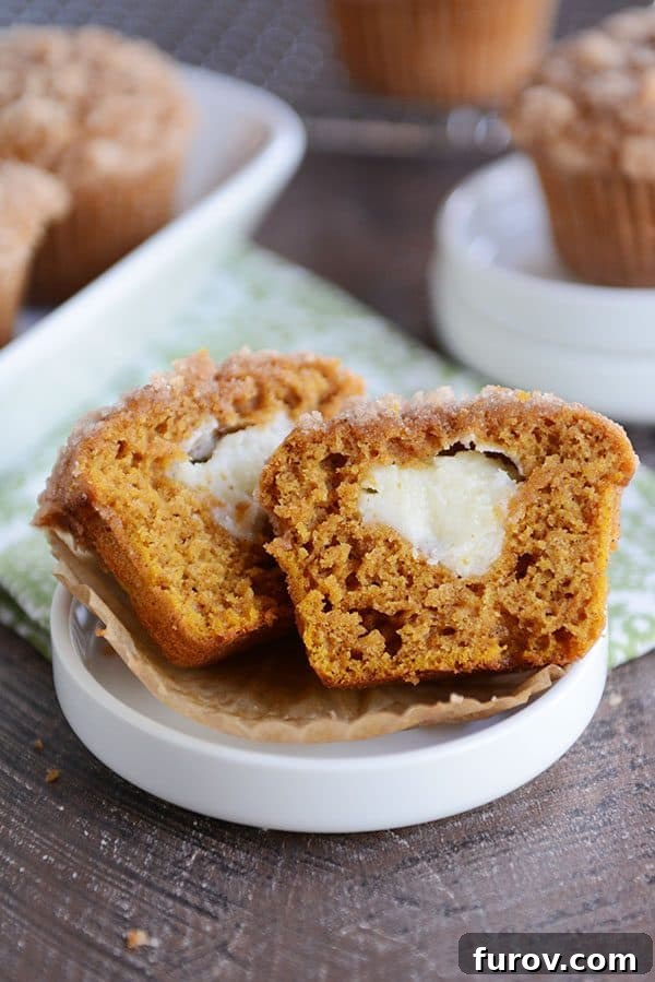 A cream cheese filled pumpkin muffin split in half on a white ramekin, showing the gooey center.