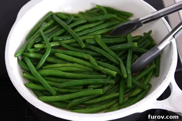 White skillet with cooked green beans, broth, and tongs, showing the finished easy skillet green beans before serving.