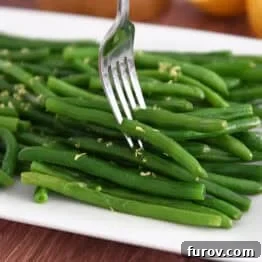 Fork piercing several fresh, cooked green beans on white tray. This image represents the final delicious outcome of the easy skillet green beans recipe.