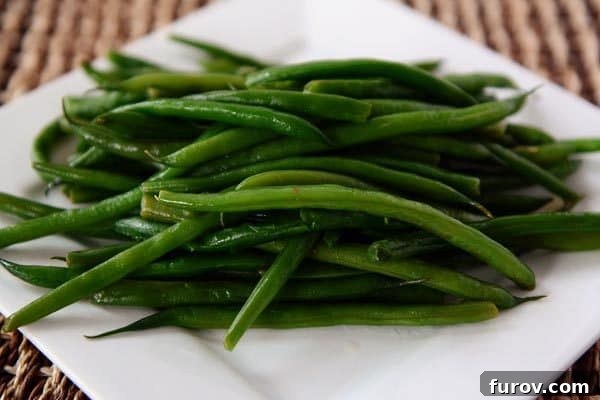 A white platter with a large serving of perfectly cooked, vibrant easy skillet green beans, garnished and ready to serve.