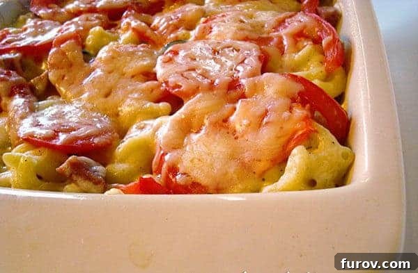 Tender elbow macaroni mixed with creamy cheese sauce and topped with sliced tomatoes, baked to golden perfection in a white ceramic dish.