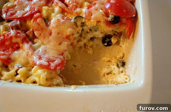 A scoop of the creamy Tuscan Macaroni and Cheese Bake with tomatoes and herbs, served in a white ceramic baking dish.