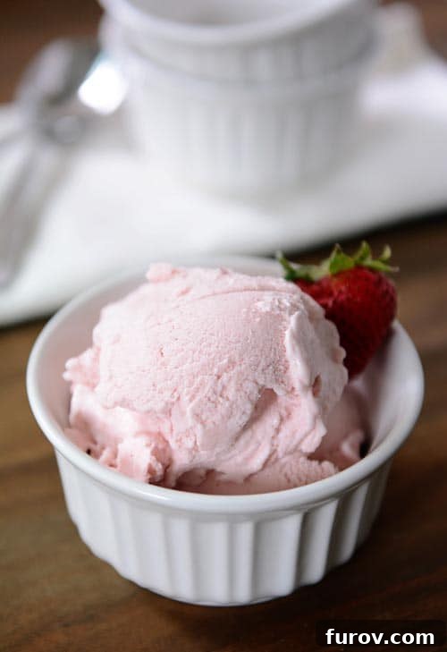 A white ramekin full of scoops of fresh strawberry gelato with a strawberry on the side, highlighting its smooth, creamy texture.