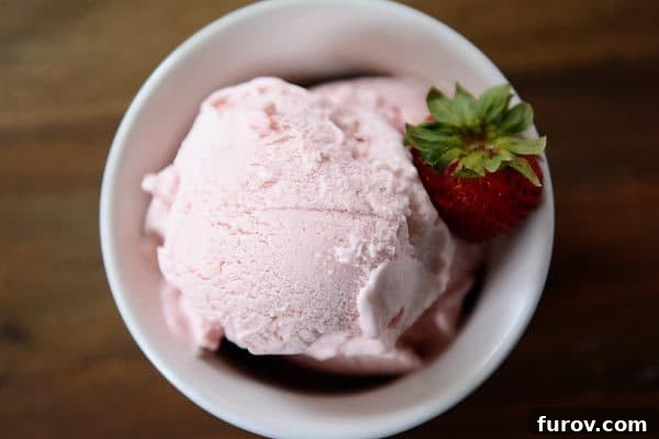 Top view of a white bowl full of fresh strawberry gelato with a strawberry on the side, emphasizing its vibrant color.