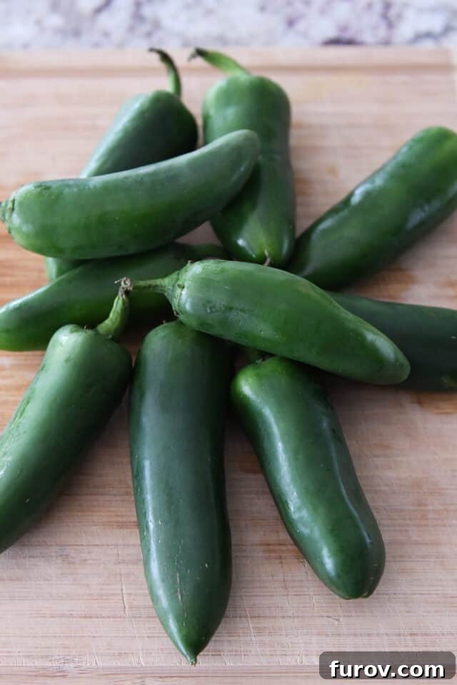 Fresh ten jalapeno peppers neatly arranged on a rustic wooden cutting board.