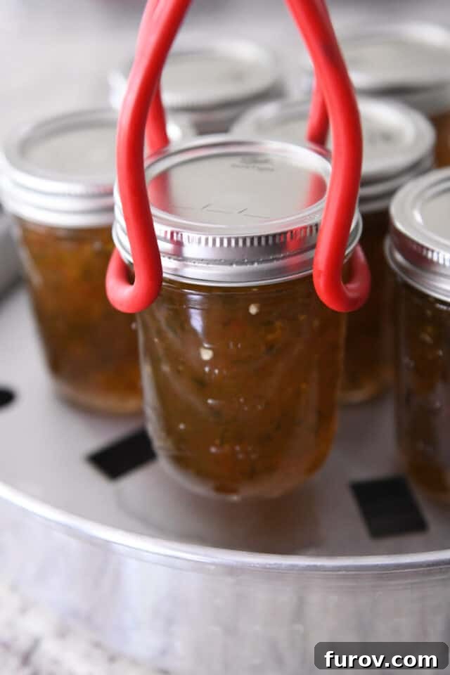 A hand carefully lifting a freshly canned jar of jalapeño jelly from a steam bath canner.