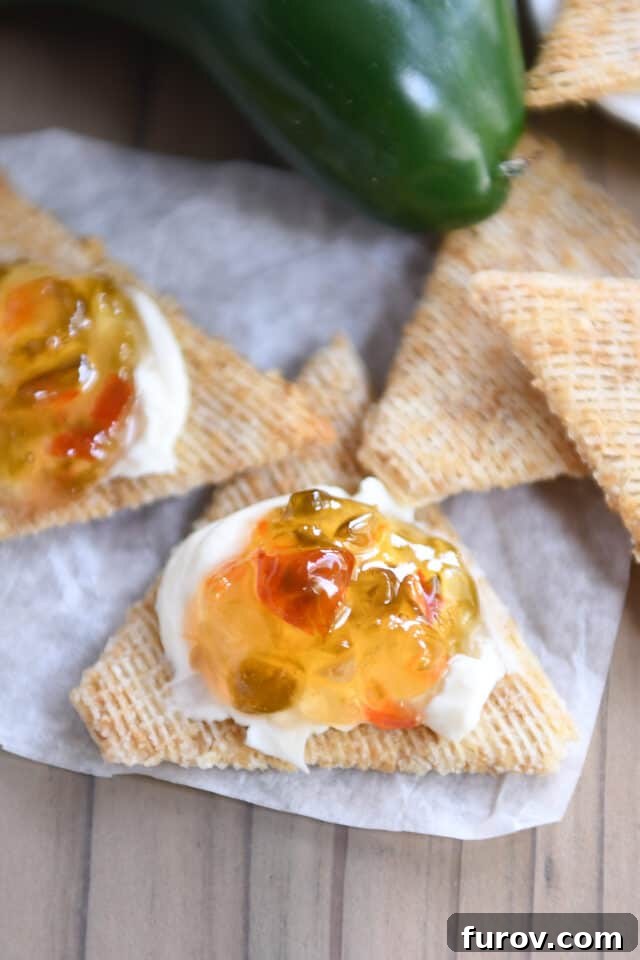 A cracker topped with smooth cream cheese and a spoonful of glistening hot pepper jelly, ready to eat.