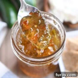 Spoon lifting up spoonful of vibrant jalapeno hot pepper jelly, showcasing its texture.