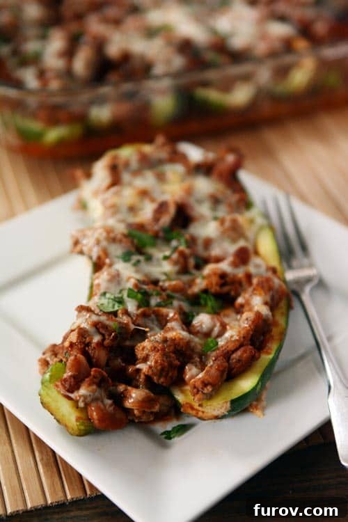 A cooked meat and cheese stuffed zucchini on a white plate.