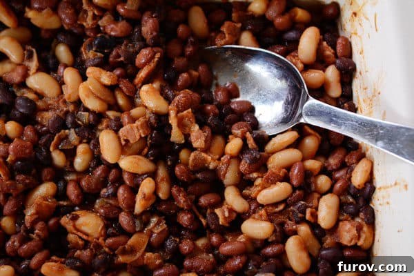 Mom's Legendary Calico Baked Beans 3 A large metal spoon stirring a generous dish of baked beans in a rustic baking pan.