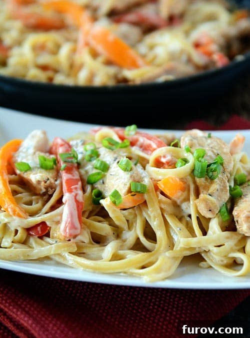 Cajun chicken pasta on a white platter with a skillet of pasta behind it.