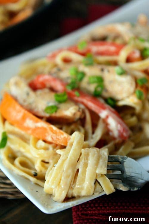A fork with creamy fettucine wrapped around it from a platter of chicken cajun pasta.