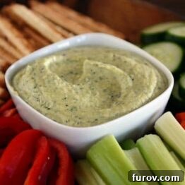 A bowl of fresh zucchini hummus, garnished with herbs and a drizzle of olive oil, ready to be served.